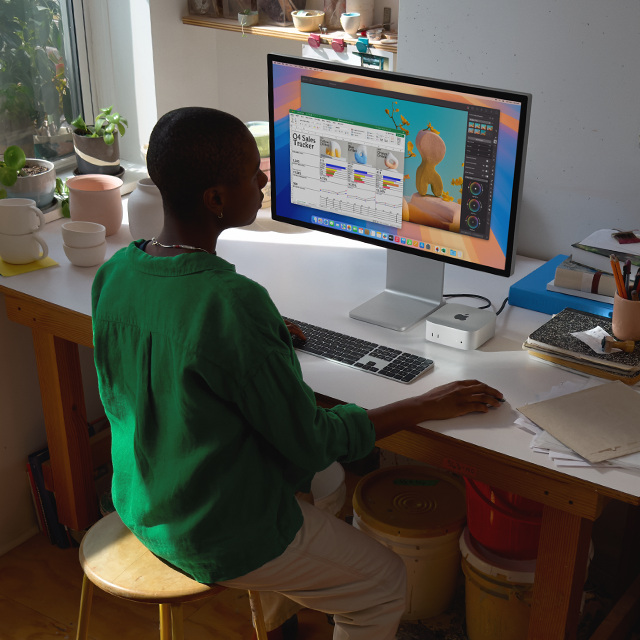 Iemand zit aan een bureau met een Mac mini en display, met op het scherm meerdere kleurrijke apps